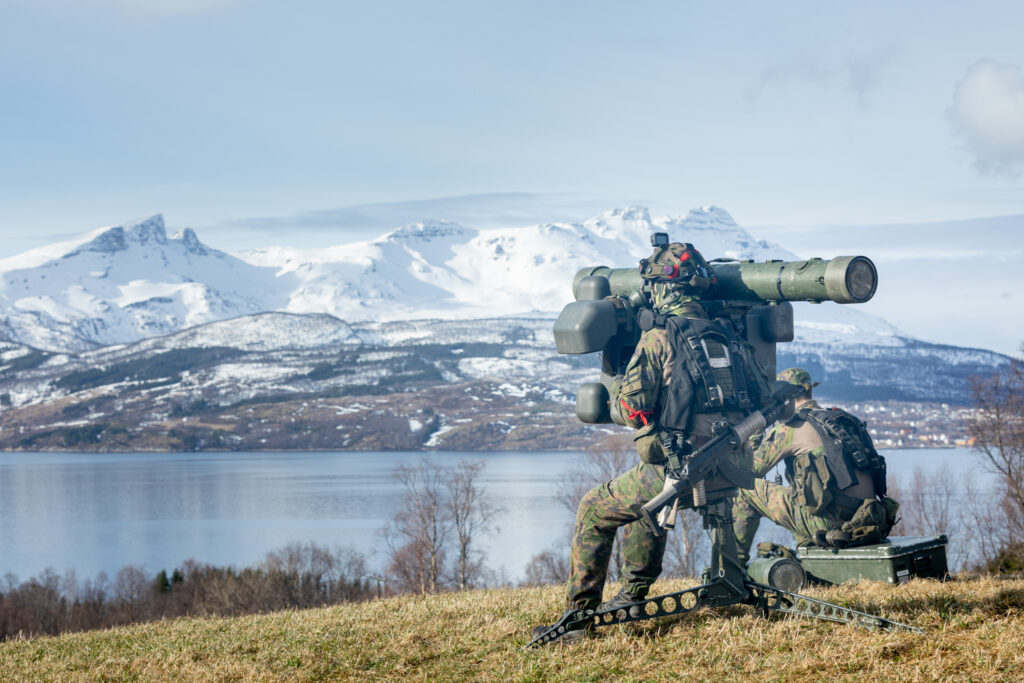 Kaksi sotilasta ja sinko veden äärellä vastarannalla luminen vuoristo